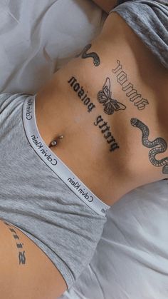 a woman laying on top of a bed with tattoos on her stomach and back side