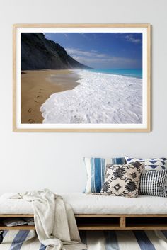 a beach scene with footprints in the sand and blue skies above it framed in wood