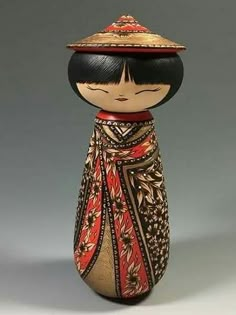 a small wooden doll wearing a red and black dress with a hat on it's head