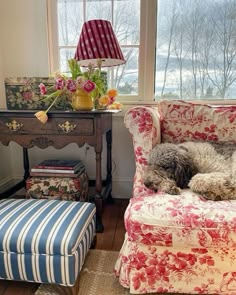 a dog laying on a chair next to a table with a lamp and flowers in it