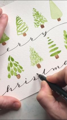 someone is writing on paper with green christmas trees