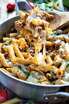 a wooden spoon full of pasta with meat and cheese on it, being lifted from a skillet