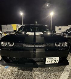 a black and white car is parked in the parking lot at night with its lights on