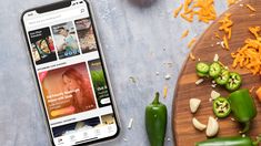 a cell phone sitting on top of a wooden cutting board next to sliced up vegetables