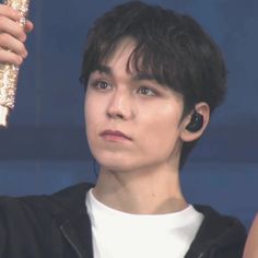 a young man holding up a pair of ear buds to his ears while wearing a black jacket