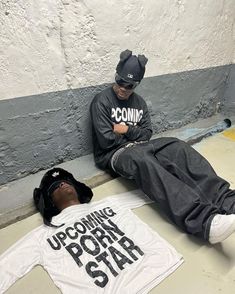 two young men sitting on the ground next to each other wearing matching t - shirts