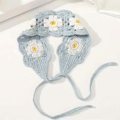 a crocheted hat with flowers on the front and side, sitting on top of a white surface