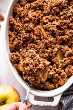 a close up of a casserole dish with apples and pecans in the background