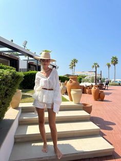 a woman standing on some steps wearing a white dress and hat with palm trees in the background