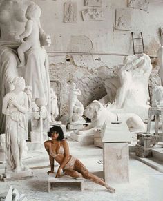 a woman is sitting on a bench in front of some white marble statues and sculptures