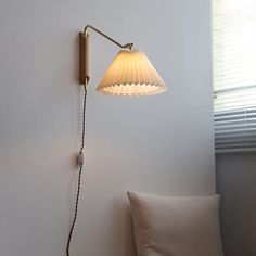 a lamp that is on the wall next to a pillow in a room with white walls