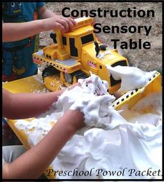 two children are playing with construction toys in the sand and water table that is made out of plastic