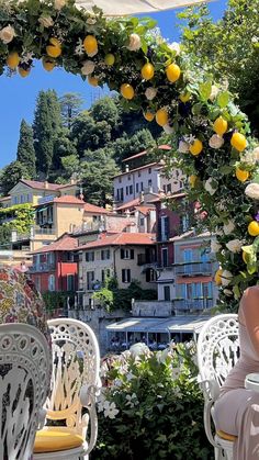 an outdoor dining area with white chairs and yellow lemons on the arch above it