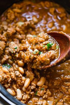 a wooden spoon scooping out some meat and beans from the slow cooked crock pot