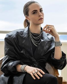 a woman sitting on top of a wooden chair wearing a black jacket and bracelets