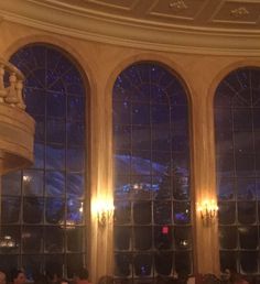 people sitting at tables in front of two large windows with lights on them and the sky outside