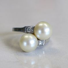 This vintage white gold ring features two large pearls at the center. Two round brilliant white diamonds are set next to them with a lovely vintage milgrain detail creating a square around each. Metal: 14K White Gold Pearls: 8.3 MM Diamonds: .10 CTW SI2 F-G Size: 5 Width: 16.5 MM @ Widest Band Width: 1.7 MM For a greater selection of jewelry please visit our website at www.BlackMarketLLC.com If you have any questions about this product or if we can help you with any of our other products please Classic Platinum Pearl Ring, Vintage White Gold Pearl Ring With Diamond Accents, Beach Rings, Etsy Gold Ring, Alternative Engagement Rings, 14k White Gold Ring, White Gold Ring, Multi Stone Ring, Wide Bands