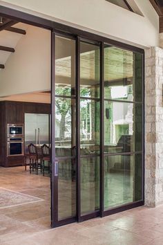 an open glass door leading to a kitchen and dining room area with large stone pillars