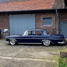 an old blue car parked in front of a brick building next to a garage door