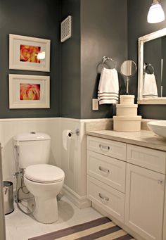 a white toilet sitting in a bathroom next to a sink under a mirror with pictures on the wall