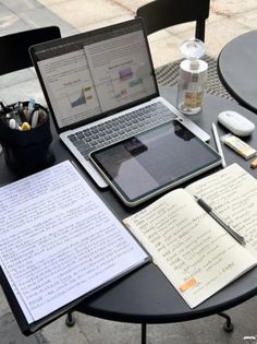 an open laptop computer sitting on top of a table next to notebooks and pens