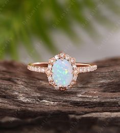 an opal and diamond ring sits on top of a piece of drift wood with leaves in the background