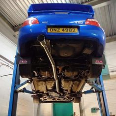 the rear end of a blue car on a lift in a garage with no one around it