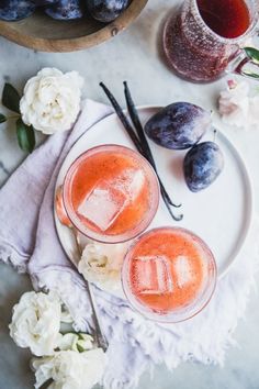 two glasses filled with liquid sitting on top of a white plate next to some flowers