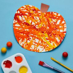 an apple shaped paper plate with paint and other art supplies next to it on a blue surface