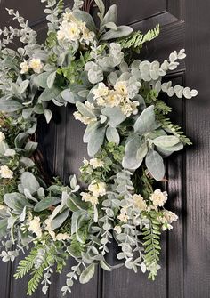 a wreath with white flowers and greenery hangs on a black wooden door, surrounded by green leaves