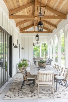 an outdoor dining table and chairs on a porch with wood beams, white walls and ceiling