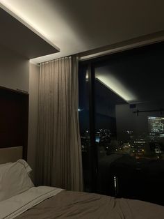 a bed sitting next to a window in a bedroom under a night sky light with the city lights behind it