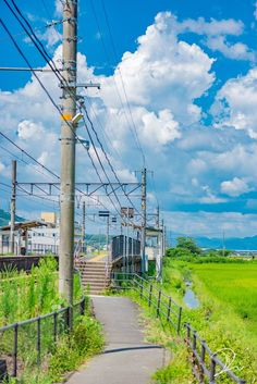 a train traveling down tracks next to a lush green field under a blue cloudy sky