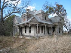 an old run down house in the middle of some tall grass and trees with no leaves on it