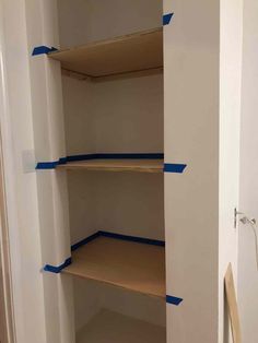 an empty closet with some blue tape on the shelves and one shelf in front of it