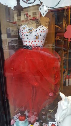 a red dress with a white crown on top and other items in the window behind it