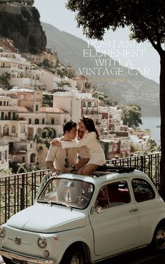 two women sitting on top of an old car in front of a cityscape