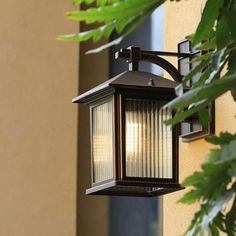 a light that is on the side of a building next to some plants and trees