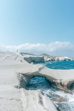 a person standing on the edge of a cliff by the ocean with an arch in the sand