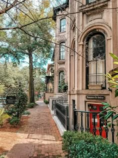 an old building with a red door and black iron fence on the sidewalk in front of it