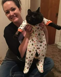 a woman is holding a black cat in her arms and smiling at the camera while she holds it up