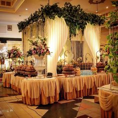 a table with many desserts on it in a banquet hall decorated with flowers and greenery