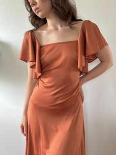 a woman in an orange dress poses for the camera with her hands on her hips