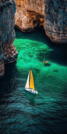 two sailboats in the water near some cliffs and green waters, with yellow sails