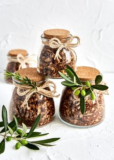 three jars filled with granola sitting on top of a white table next to an olive branch