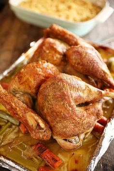 a roasted chicken with vegetables and gravy in a foil container on a wooden table