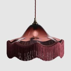 a pink hanging light with fringes on it's sides and a black base