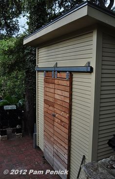 a small shed with a wooden door on the side and brick walkway leading up to it