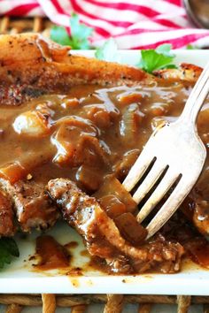 a white plate topped with meat covered in gravy and a fork on top of it