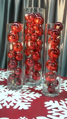 three clear vases with red balls in them on a tablecloth covered table cloth